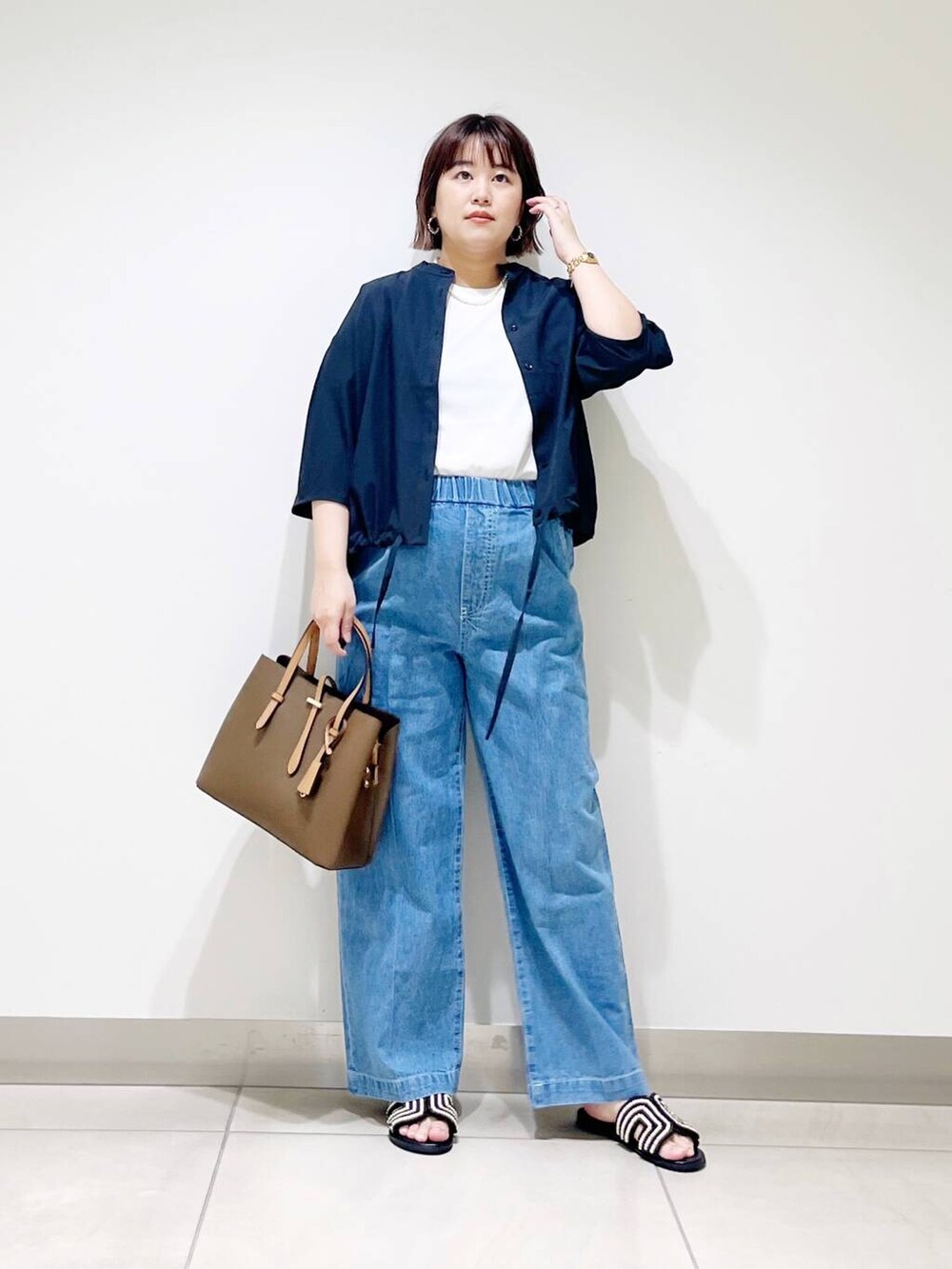 ブラウン系のトートバッグ、ブルー系のデニムパンツ、ブラック系のサンダルを着用したレディースの春コーディネートの8枚目の写真