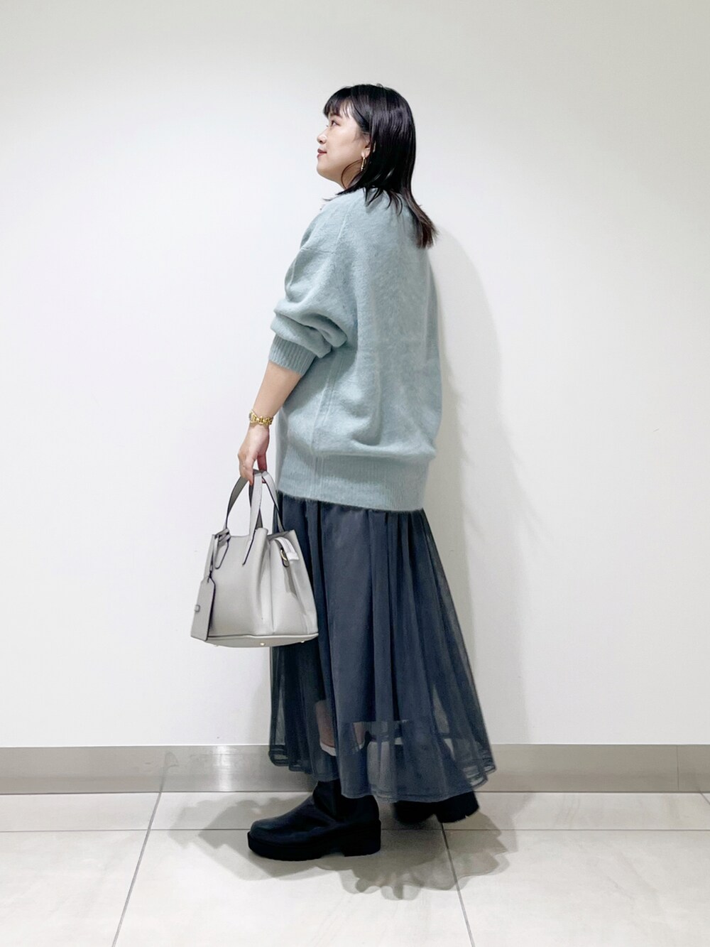 グリーン系のニット/セーター、グレー系のスカート、グレー系のトートバッグを着用したレディースの秋コーディネートの4枚目の写真