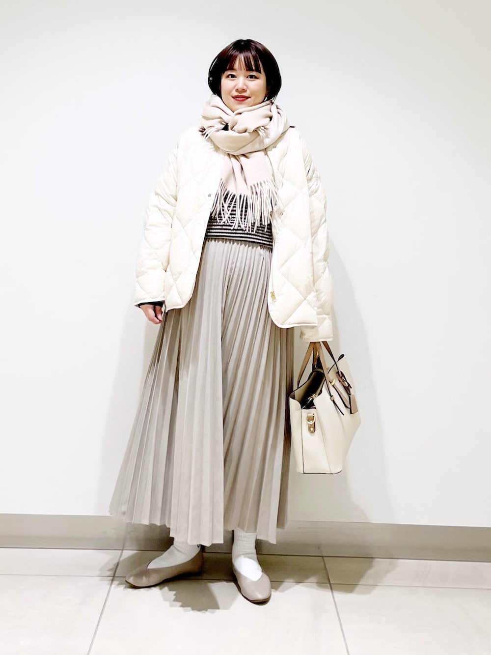 ホワイト系のダウンジャケット/コート、グレー系のニット/セーター、ベージュ系のスカートを着用したレディースの冬コーディネートの2枚目の写真