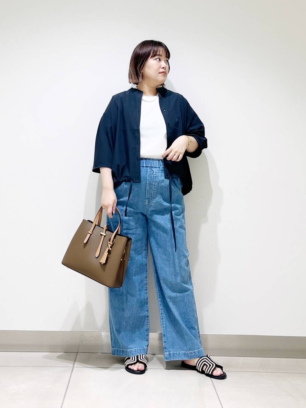 ブラウン系のトートバッグ、ブルー系のデニムパンツ、ブラック系のサンダルを着用したレディースの春コーディネートの2枚目の写真