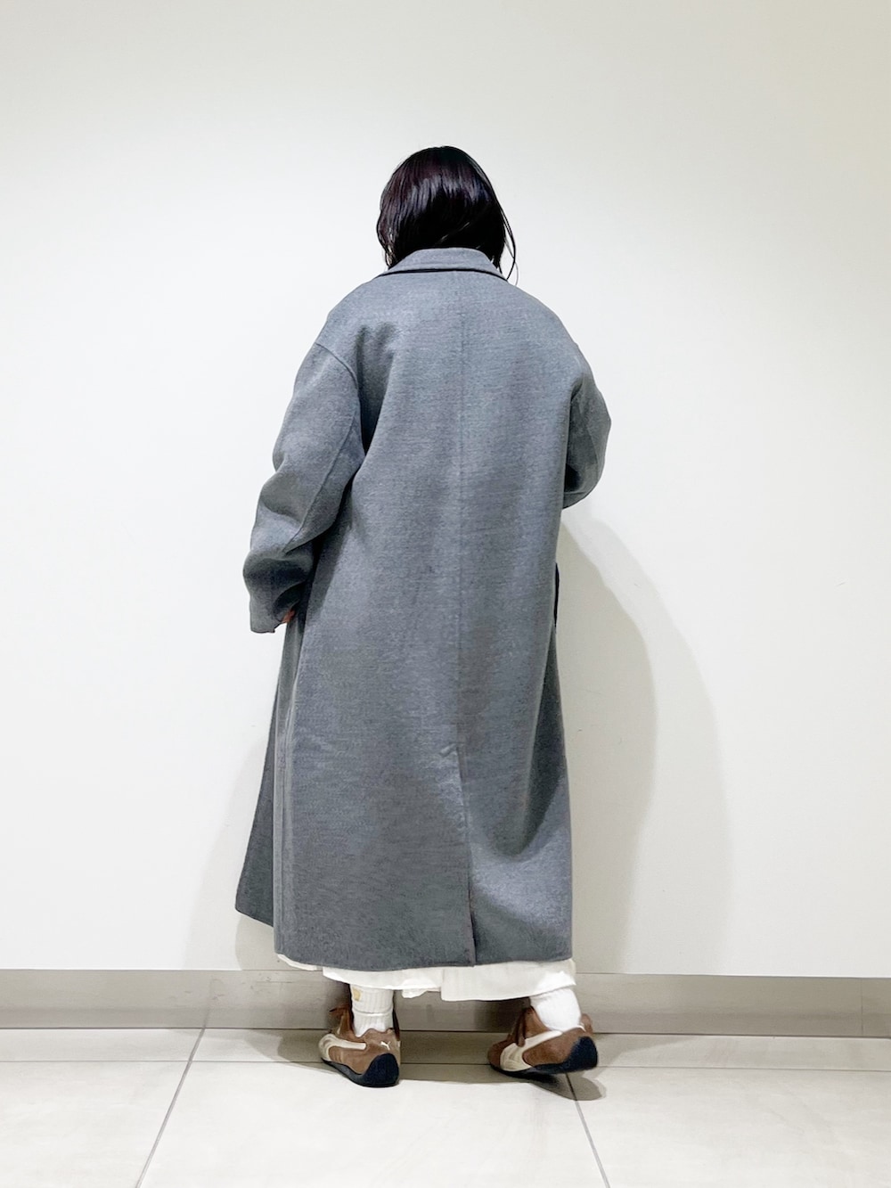 ブルー系のニット/セーター、ホワイト系のスカート、ブラック系のスニーカーを着用したレディースの秋コーディネートの5枚目の写真