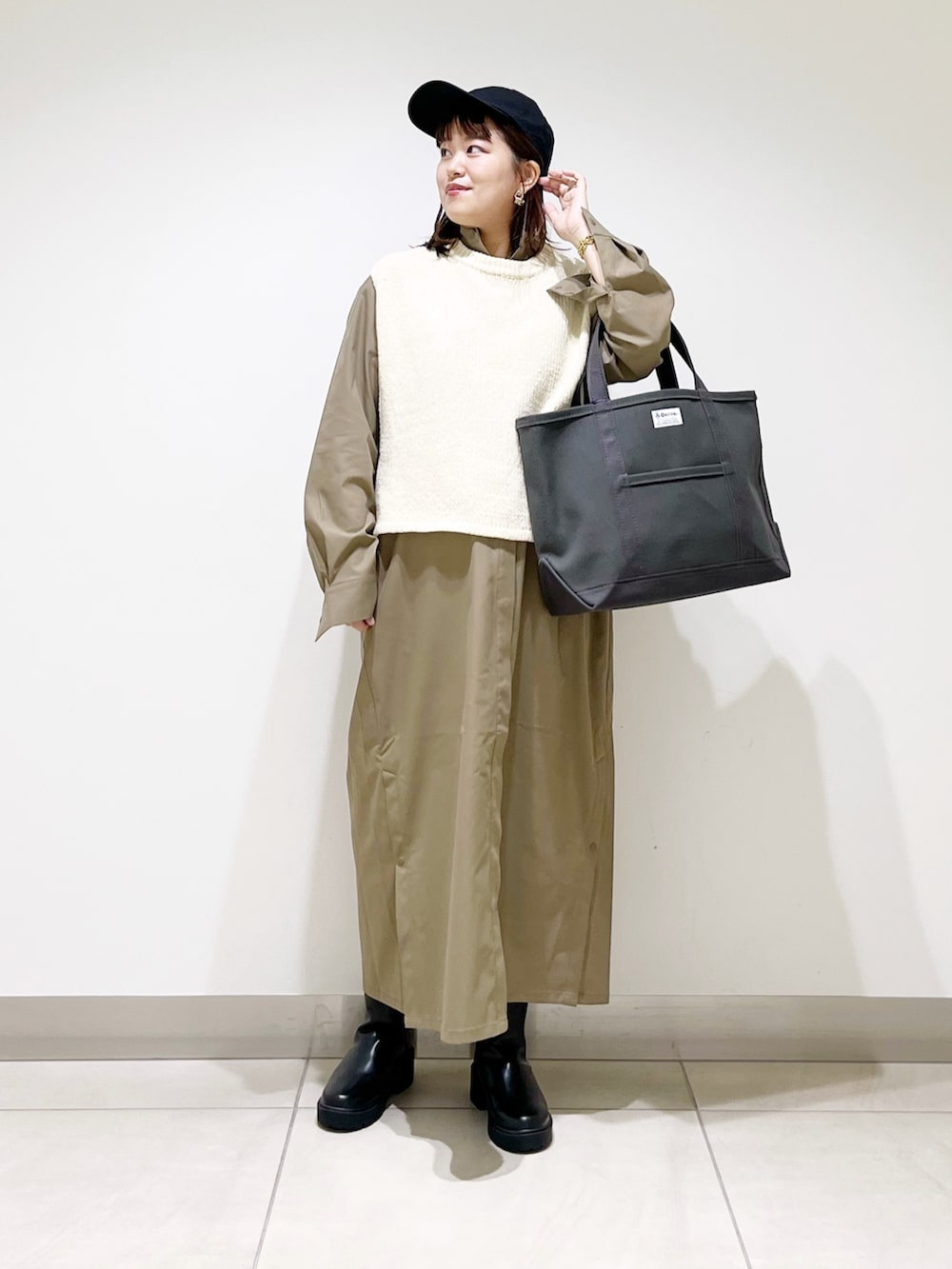 ホワイト系のベスト、グリーン系のワンピース、グレー系のトートバッグを着用したレディースの秋コーディネートの3枚目の写真