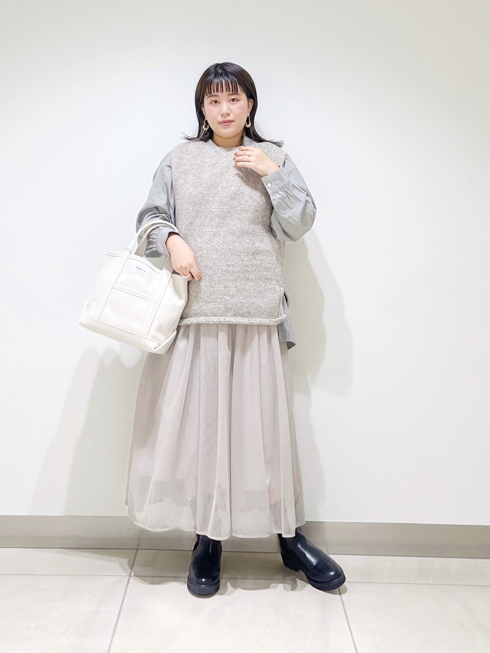 グレー系のニット/セーター、ホワイト系のトートバッグ、グレー系のスカートを着用したレディースの秋コーディネートの3枚目の写真