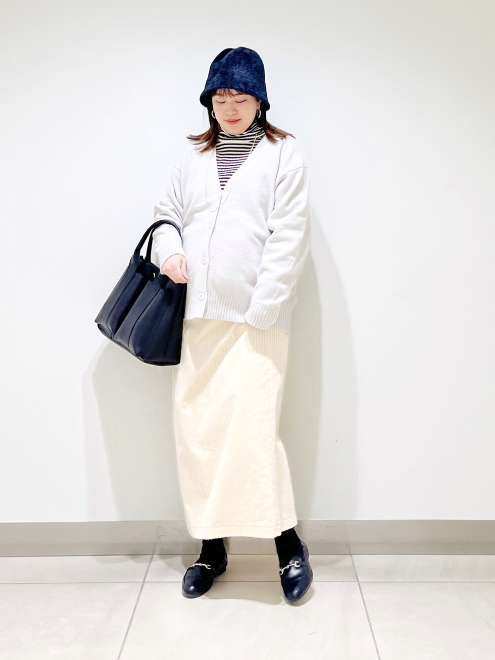 グレー系のニット/セーター、ホワイト系のカーディガン/ボレロ、ブラック系のトートバッグを着用したレディースの冬コーディネートの3枚目の写真