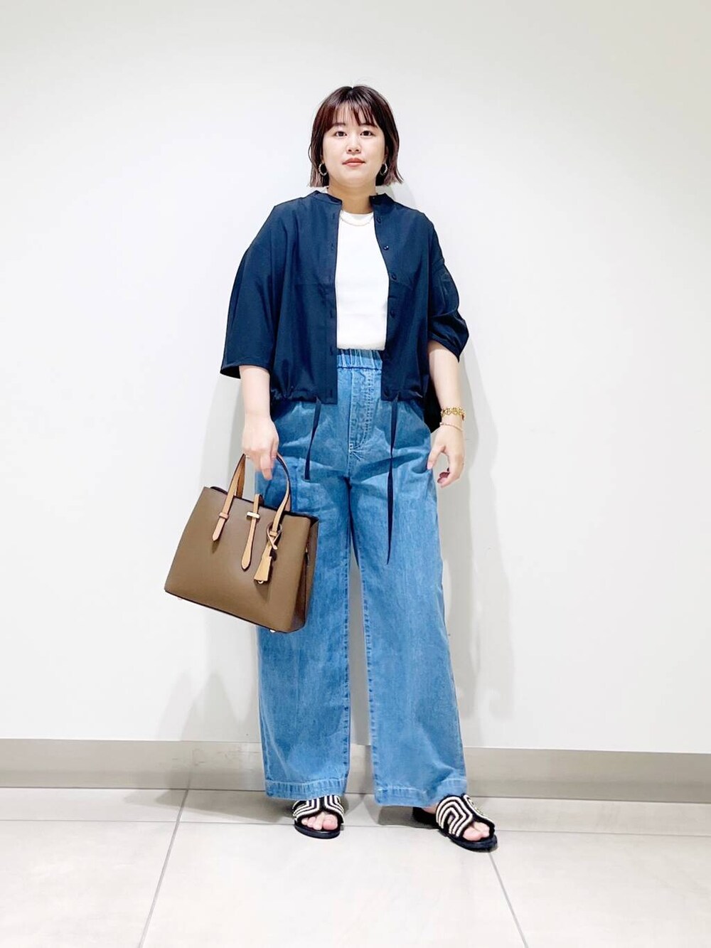 ブラウン系のトートバッグ、ブルー系のデニムパンツ、ブラック系のサンダルを着用したレディースの春コーディネートの10枚目の写真