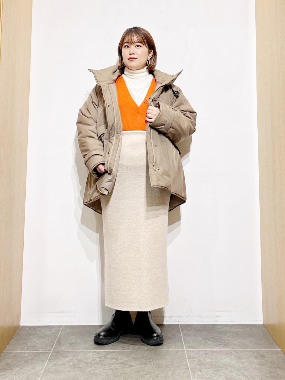 ベージュ系のダウンジャケット/コート、オレンジ系のベスト、ホワイト系のニット/セーターを着用したレディースの冬コーディネートの3枚目の写真