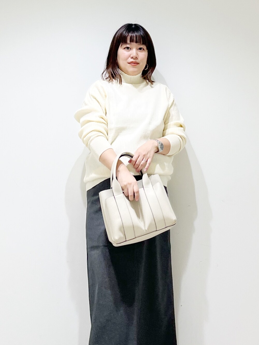 ホワイト系のニット/セーター、ホワイト系のトートバッグ、グレー系のスカートを着用したレディースの秋コーディネートの4枚目の写真
