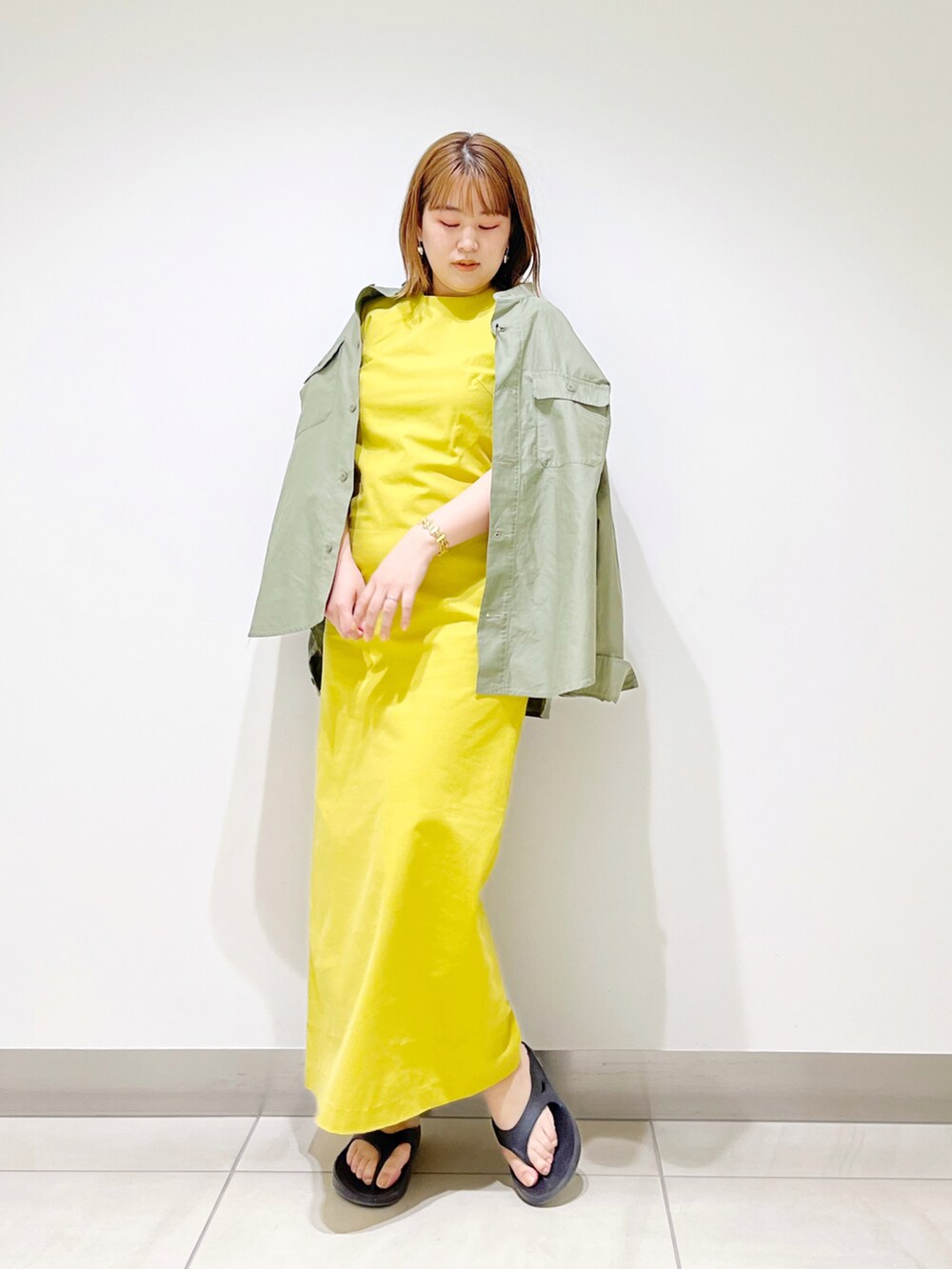 イエロー系のワンピース、グリーン系のシャツ/ブラウス、ブラック系のサンダルを着用したレディースの春コーディネートの3枚目の写真