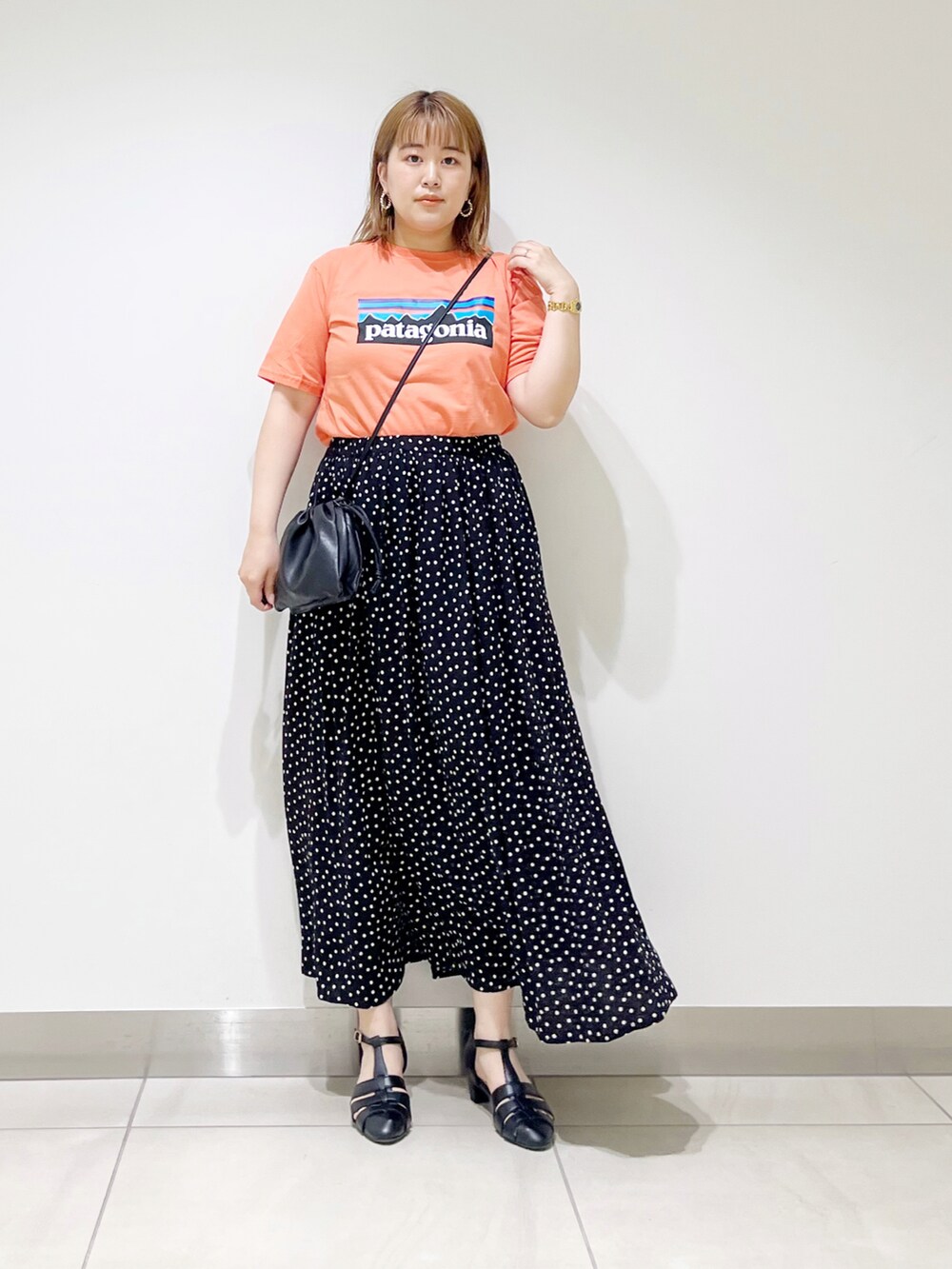 オレンジ系のTシャツ/カットソー、ブラック系のスカート、ブラック系のサンダルを着用したレディースの春コーディネートの2枚目の写真