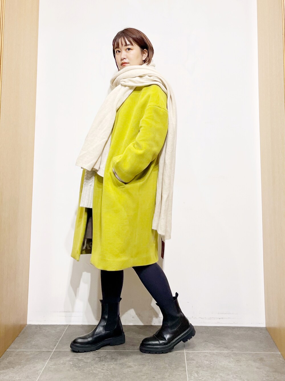 イエロー系のその他アウター、ホワイト系のニット/セーター、ブラック系のブーツを着用したレディースの冬コーディネートの3枚目の写真