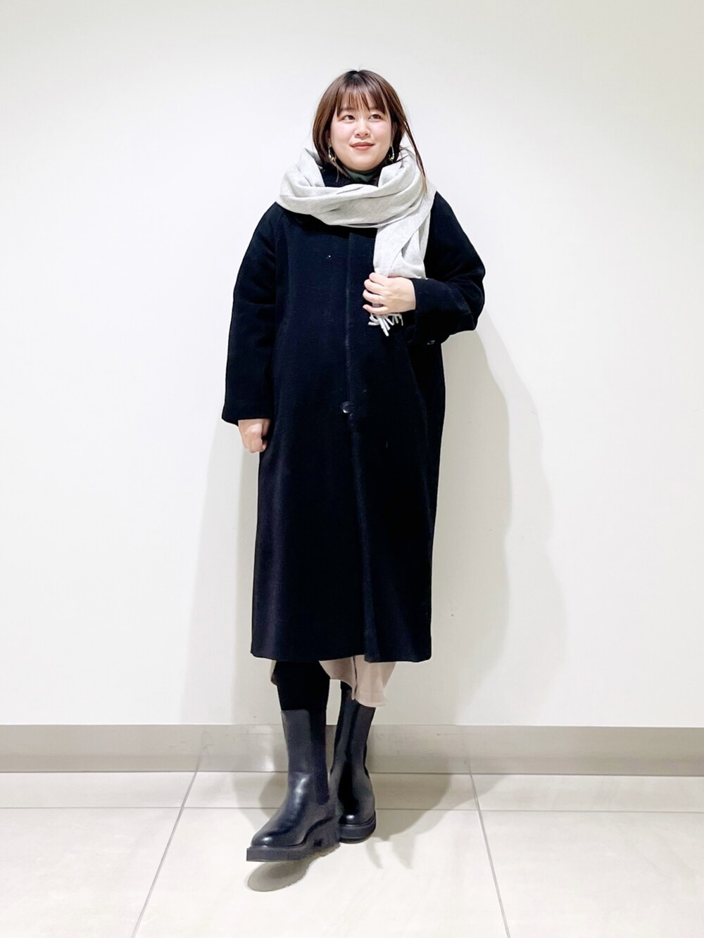 ベージュ系のワンピース、ブラック系のブーツ、ブラック系のステンカラーコートを着用したレディースの冬コーディネートの6枚目の写真