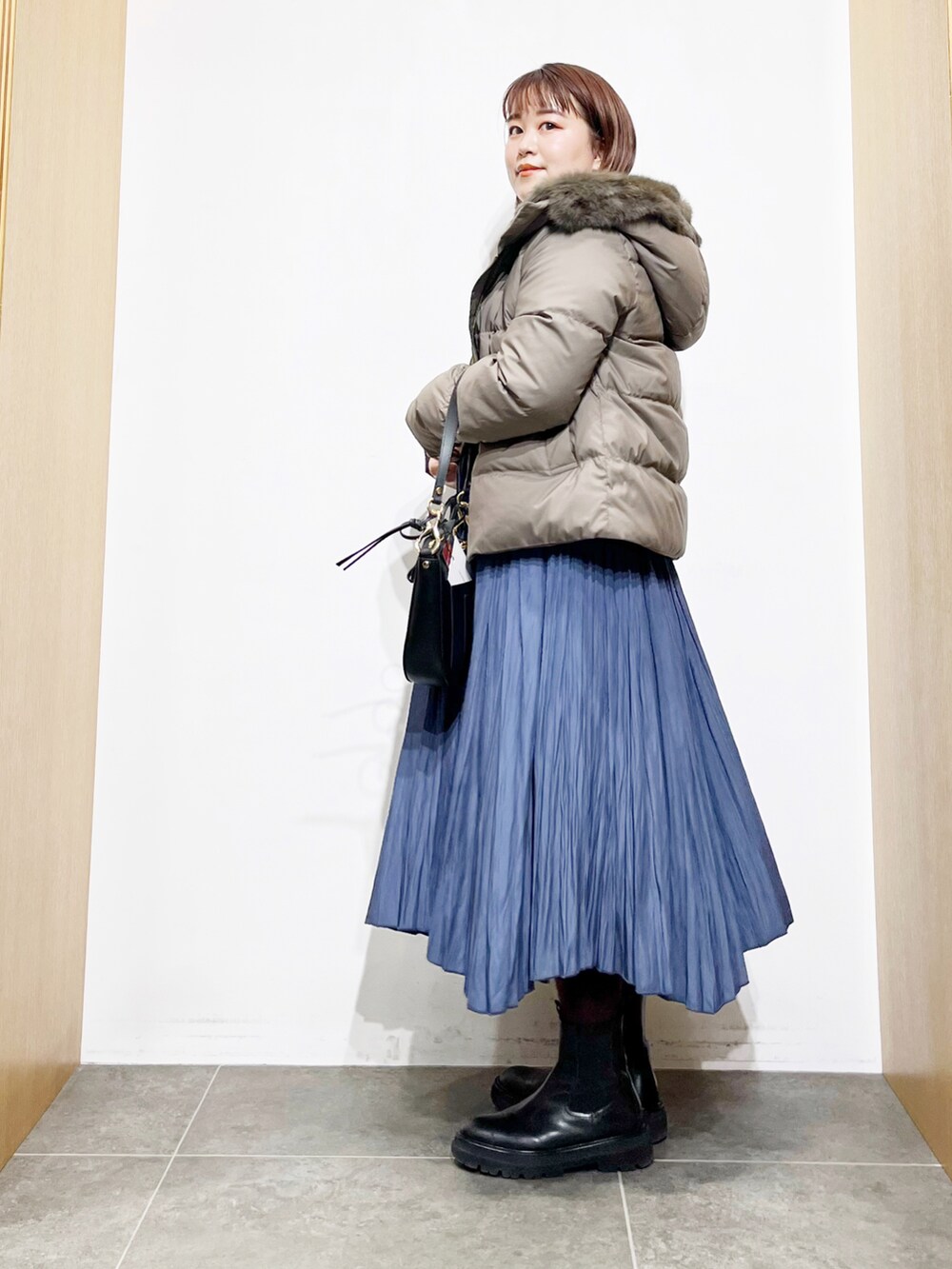 グリーン系のダウンジャケット/コート、ベージュ系のニット/セーター、ブラック系のショルダーバッグを着用したレディースの冬コーディネートの3枚目の写真