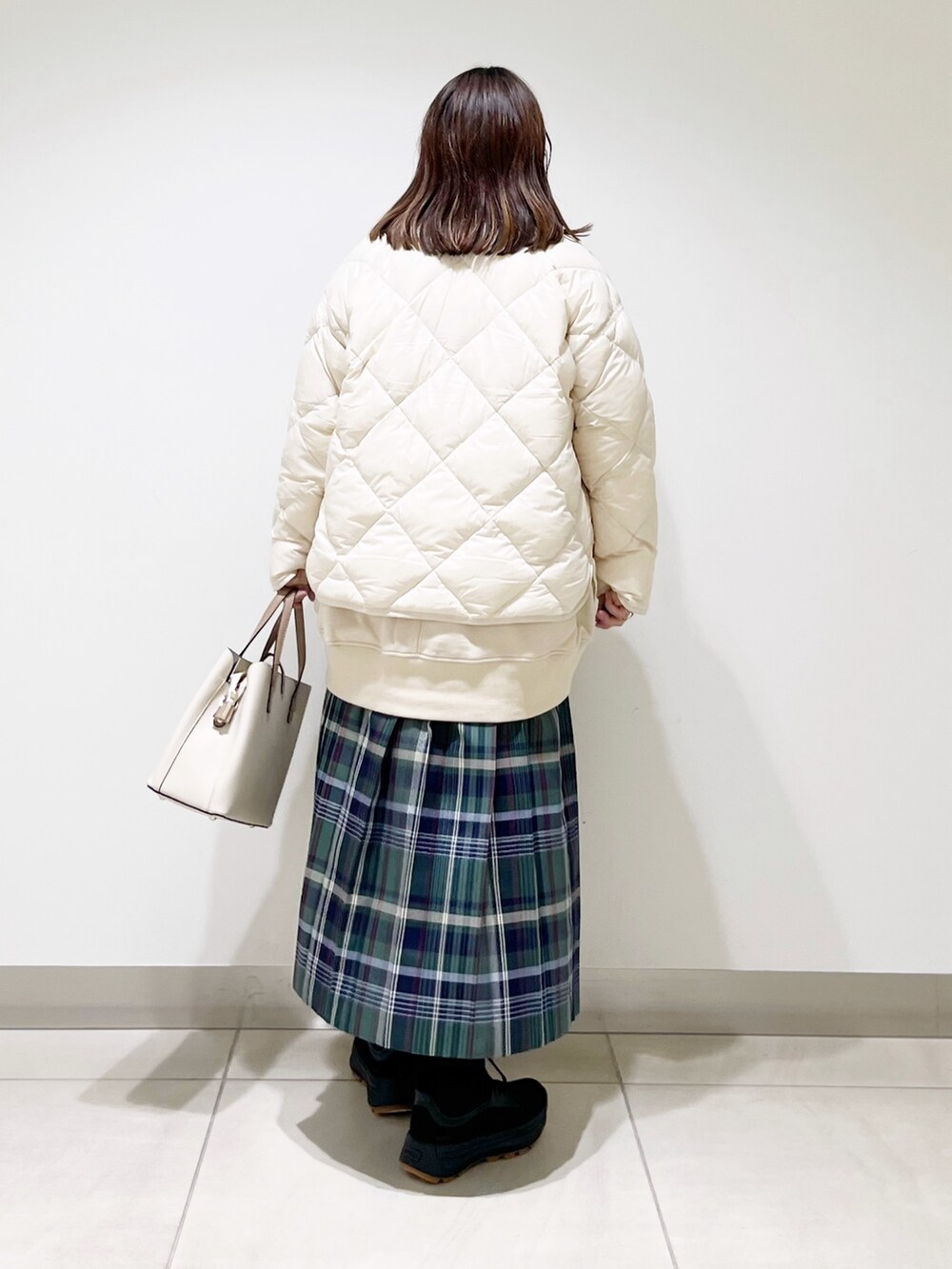 ベージュ系のスウェット、ホワイト系のダウンジャケット/コート、グリーン系のスカートを着用したレディースの秋コーディネートの7枚目の写真