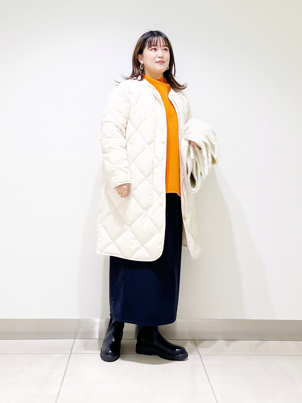 ベージュ系のダウンジャケット/コート、オレンジ系のニット/セーター、ブルー系のスカートを着用したレディースの秋コーディネートの4枚目の写真