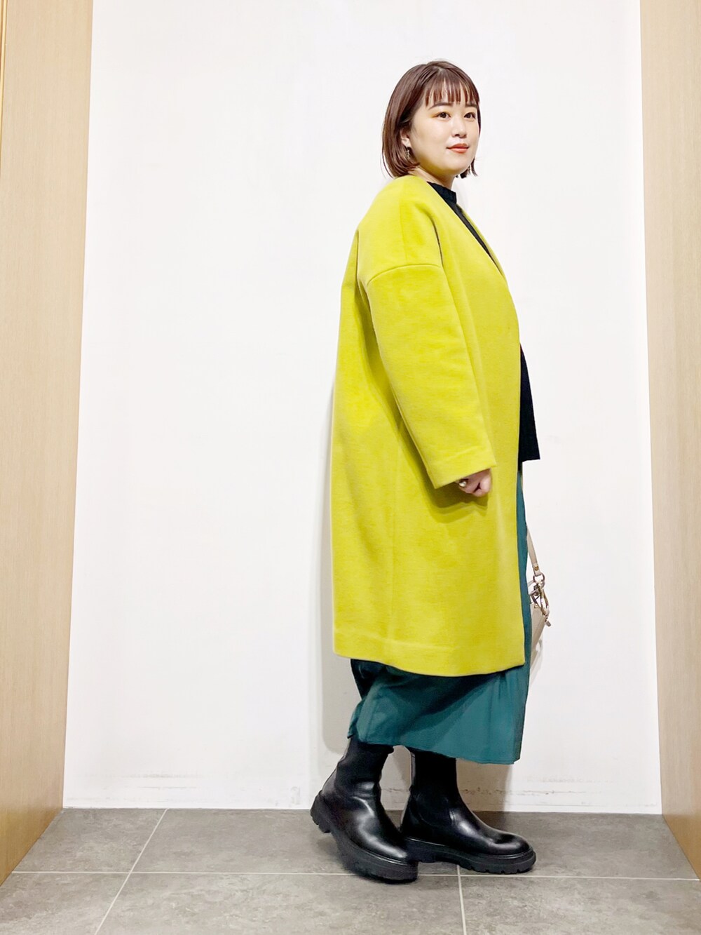 ブラック系のニット/セーター、イエロー系のその他アウター、グリーン系のスカートを着用したレディースの冬コーディネートの2枚目の写真