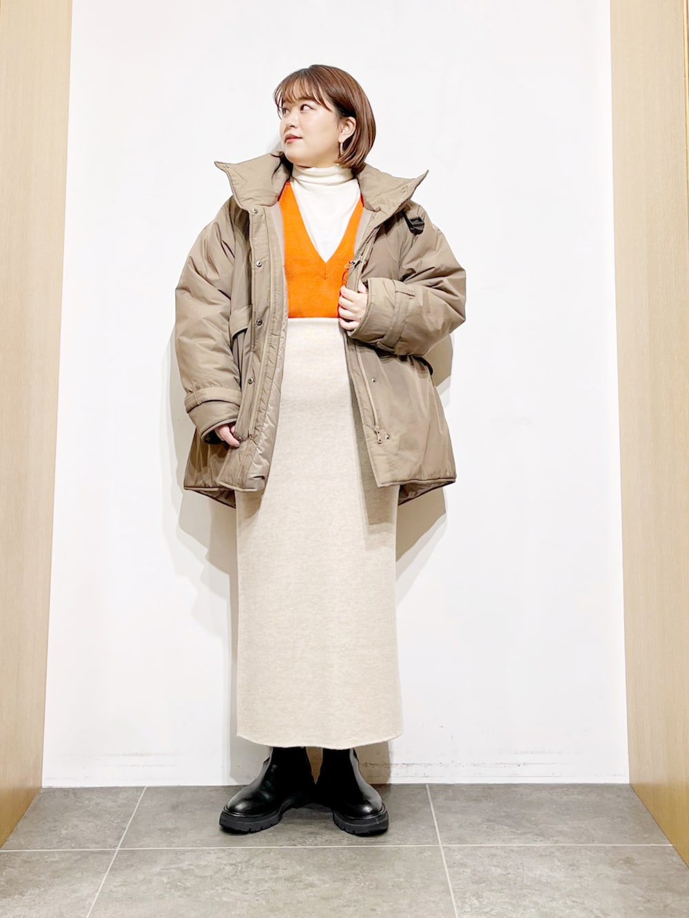 ベージュ系のダウンジャケット/コート、オレンジ系のベスト、ホワイト系のニット/セーターを着用したレディースの冬コーディネートの4枚目の写真