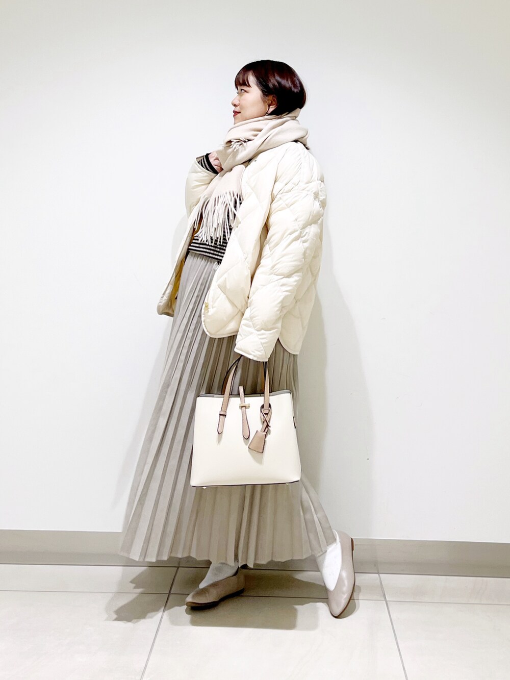 ホワイト系のダウンジャケット/コート、グレー系のニット/セーター、ベージュ系のスカートを着用したレディースの冬コーディネートの3枚目の写真