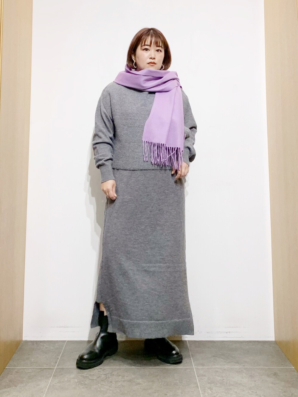 グレー系のワンピース、ブラック系のブーツ、パープル系のマフラーを着用したレディースの冬コーディネートの2枚目の写真