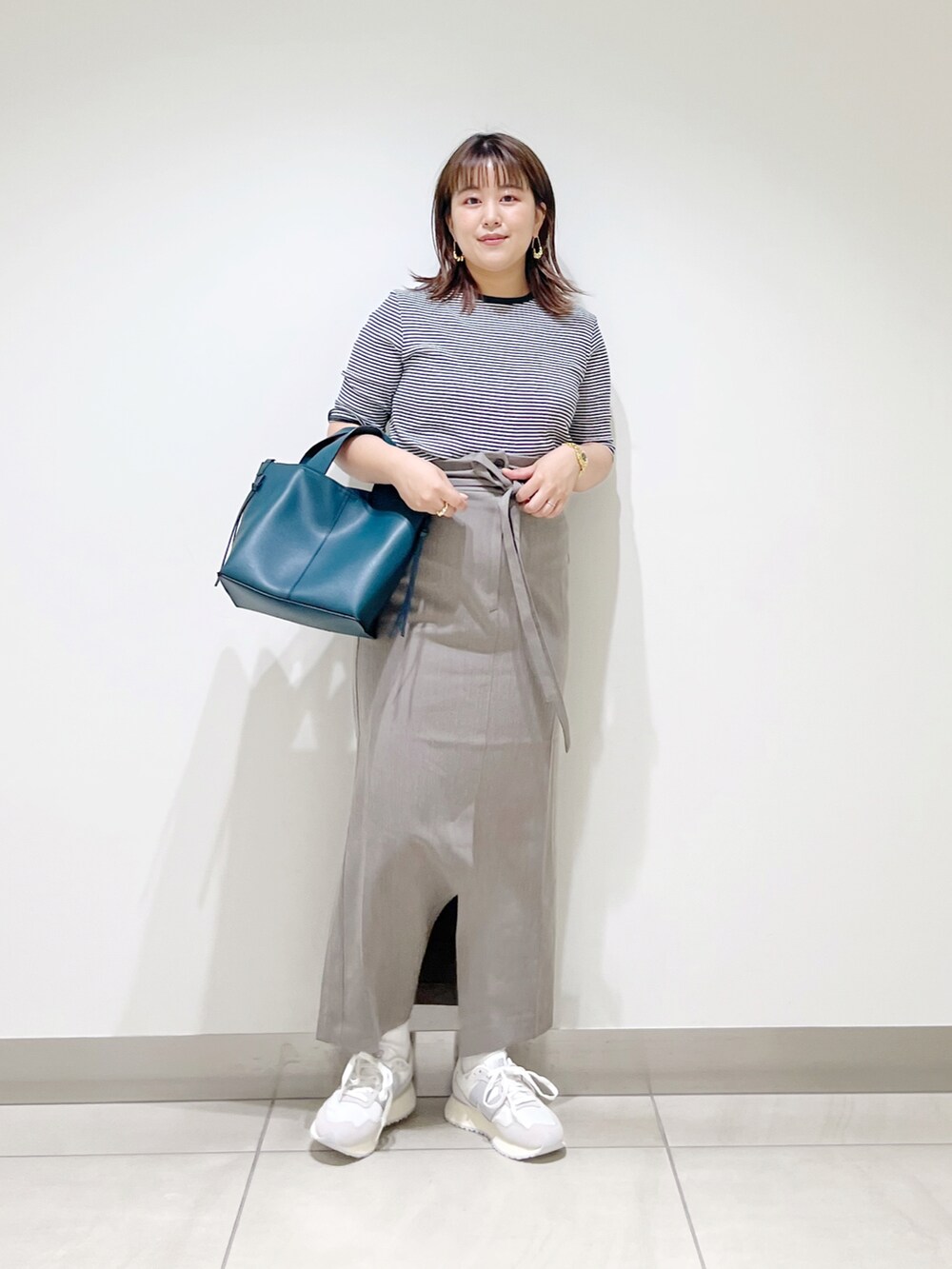 ブラウン系のスカート、ブルー系のトートバッグ、ホワイト系のスニーカーを着用したレディースの夏コーディネートの2枚目の写真