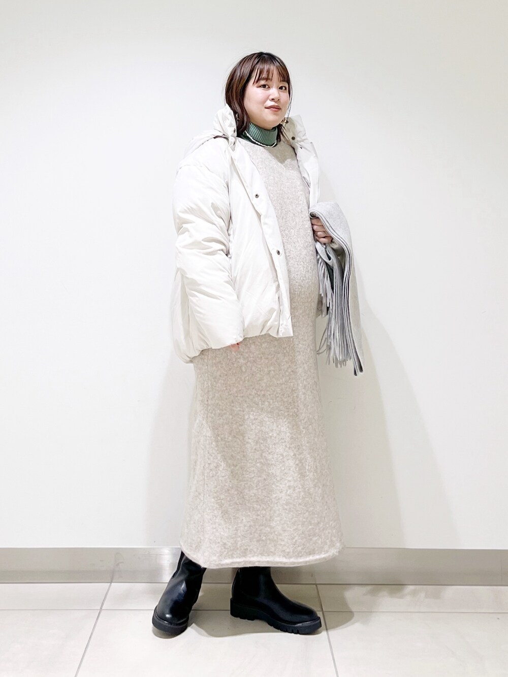 ホワイト系のダウンジャケット/コート、ベージュ系のワンピース、グリーン系のニット/セーターを着用したレディースの冬コーディネートの6枚目の写真
