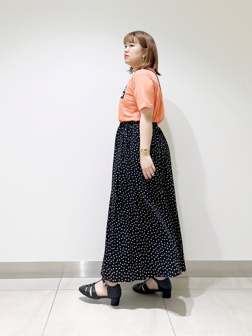 オレンジ系のTシャツ/カットソー、ブラック系のスカート、ブラック系のサンダルを着用したレディースの春コーディネートの4枚目の写真