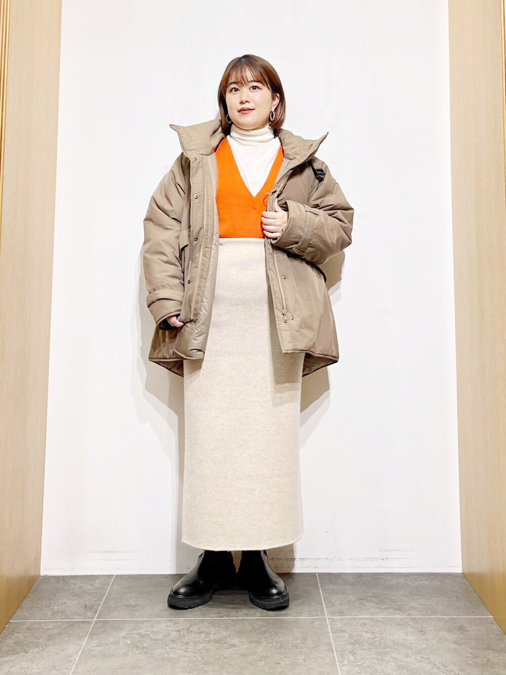 ベージュ系のダウンジャケット/コート、オレンジ系のベスト、ホワイト系のニット/セーターを着用したレディースの冬コーディネートの5枚目の写真