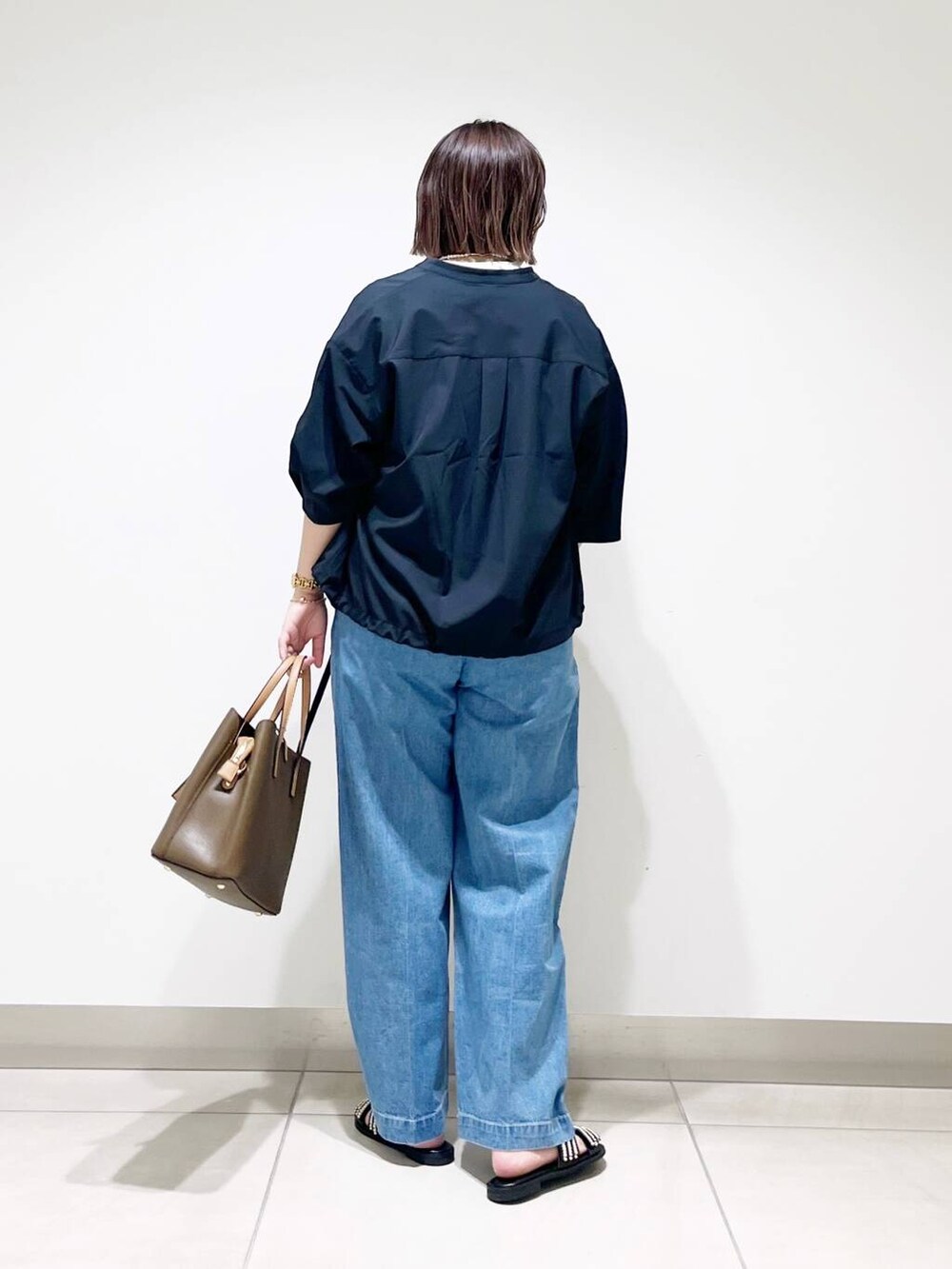 ブラウン系のトートバッグ、ブルー系のデニムパンツ、ブラック系のサンダルを着用したレディースの春コーディネートの6枚目の写真