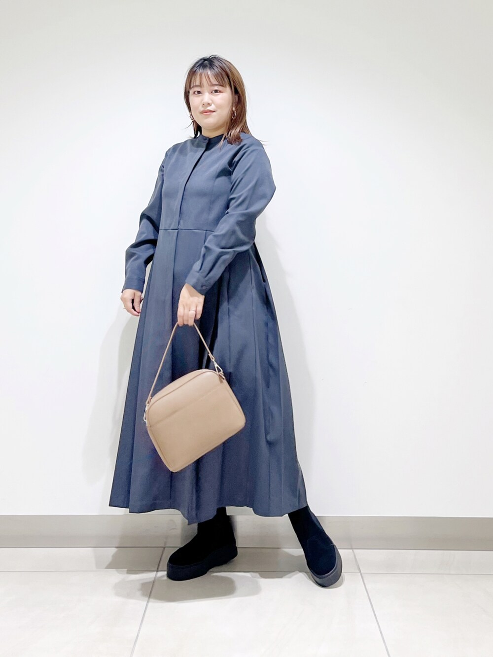 グレー系のワンピース、ブラウン系のショルダーバッグ、ブラック系のブーツを着用したレディースの秋コーディネートの3枚目の写真