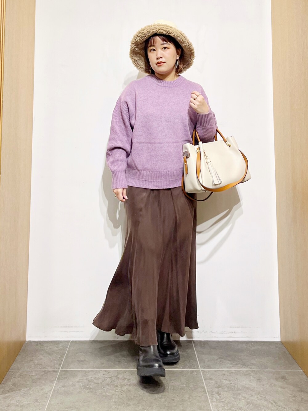 パープル系のニット/セーター、ブラウン系のスカート、ホワイト系のトートバッグを着用したレディースの冬コーディネートの3枚目の写真