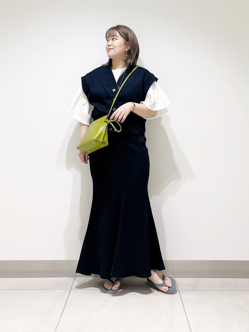 ブラック系のベスト、ブラック系のスカート、グリーン系のショルダーバッグを着用したレディースの春コーディネートの2枚目の写真