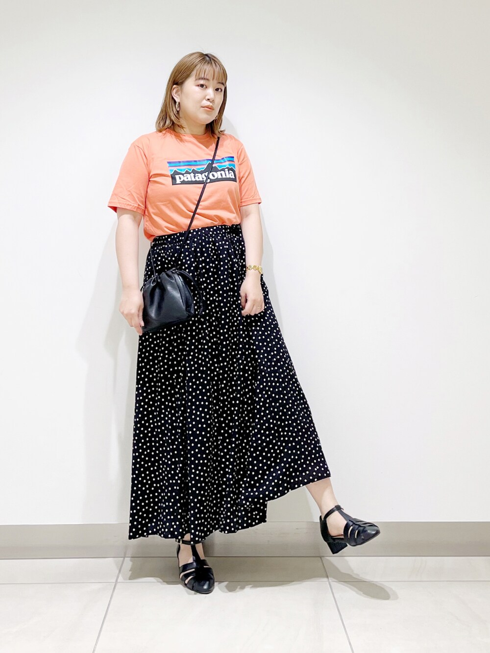 オレンジ系のTシャツ/カットソー、ブラック系のスカート、ブラック系のサンダルを着用したレディースの春コーディネートの3枚目の写真