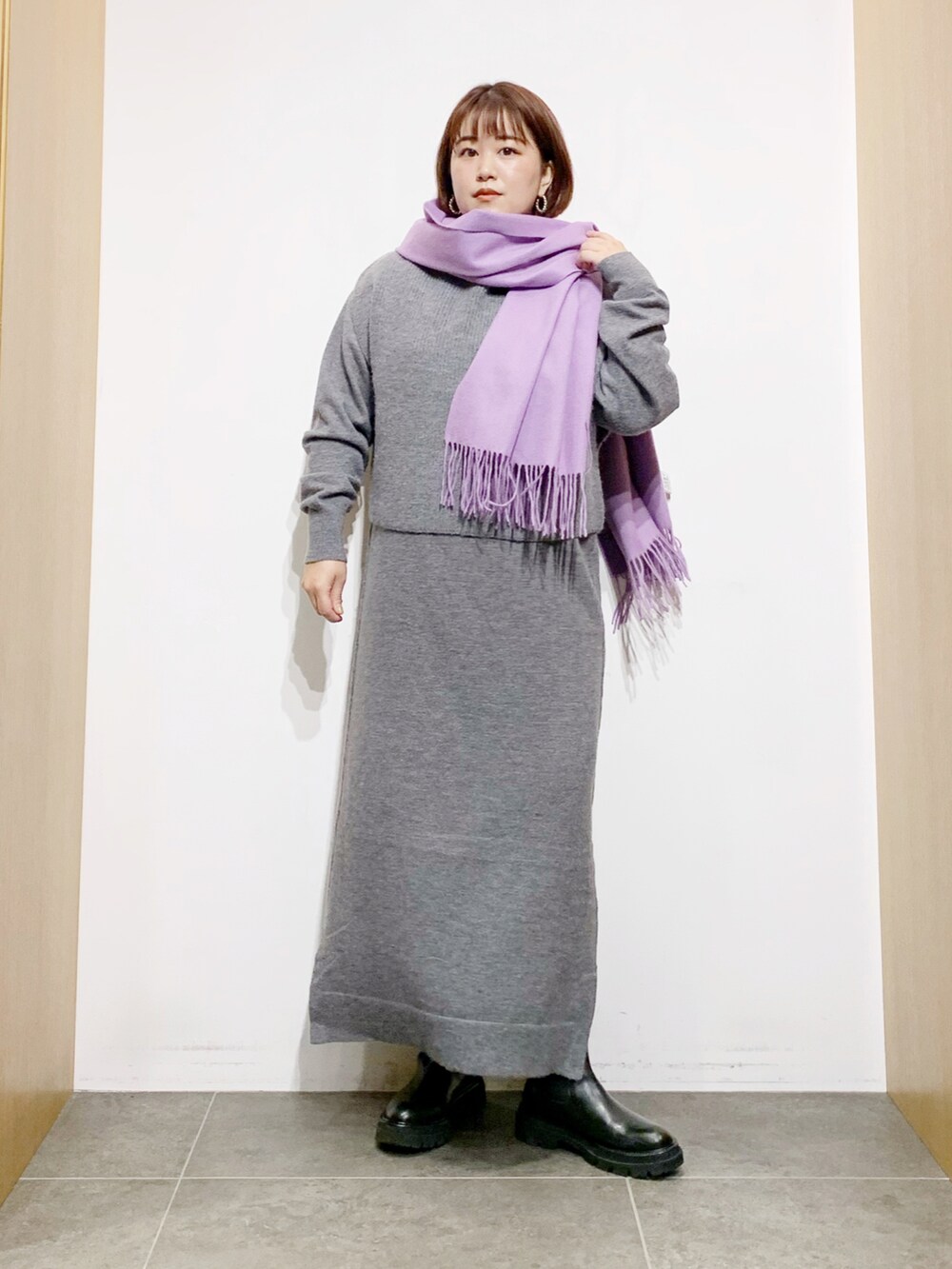 グレー系のワンピース、ブラック系のブーツ、パープル系のマフラーを着用したレディースの冬コーディネートの4枚目の写真