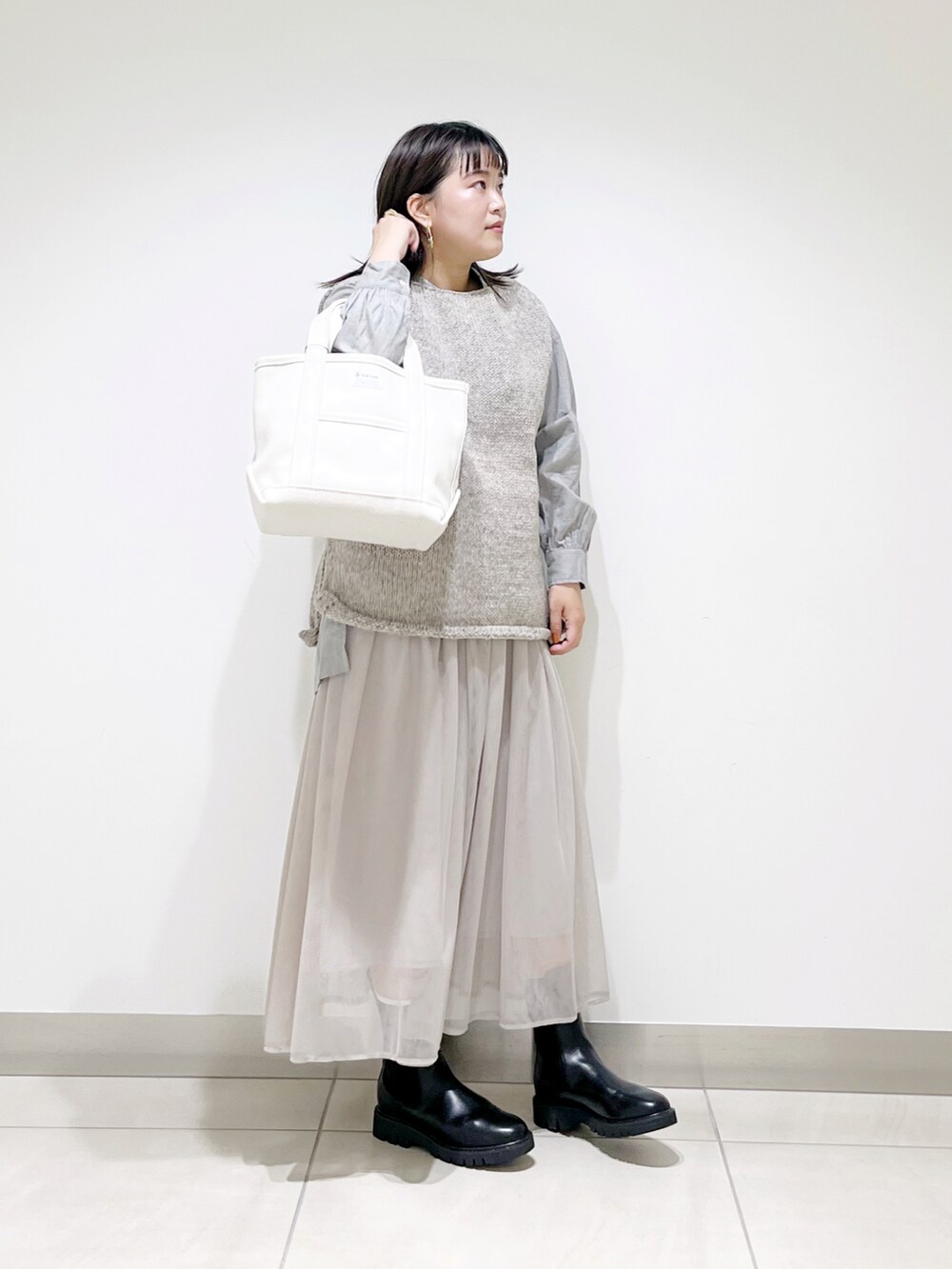 グレー系のニット/セーター、ホワイト系のトートバッグ、グレー系のスカートを着用したレディースの秋コーディネートの5枚目の写真