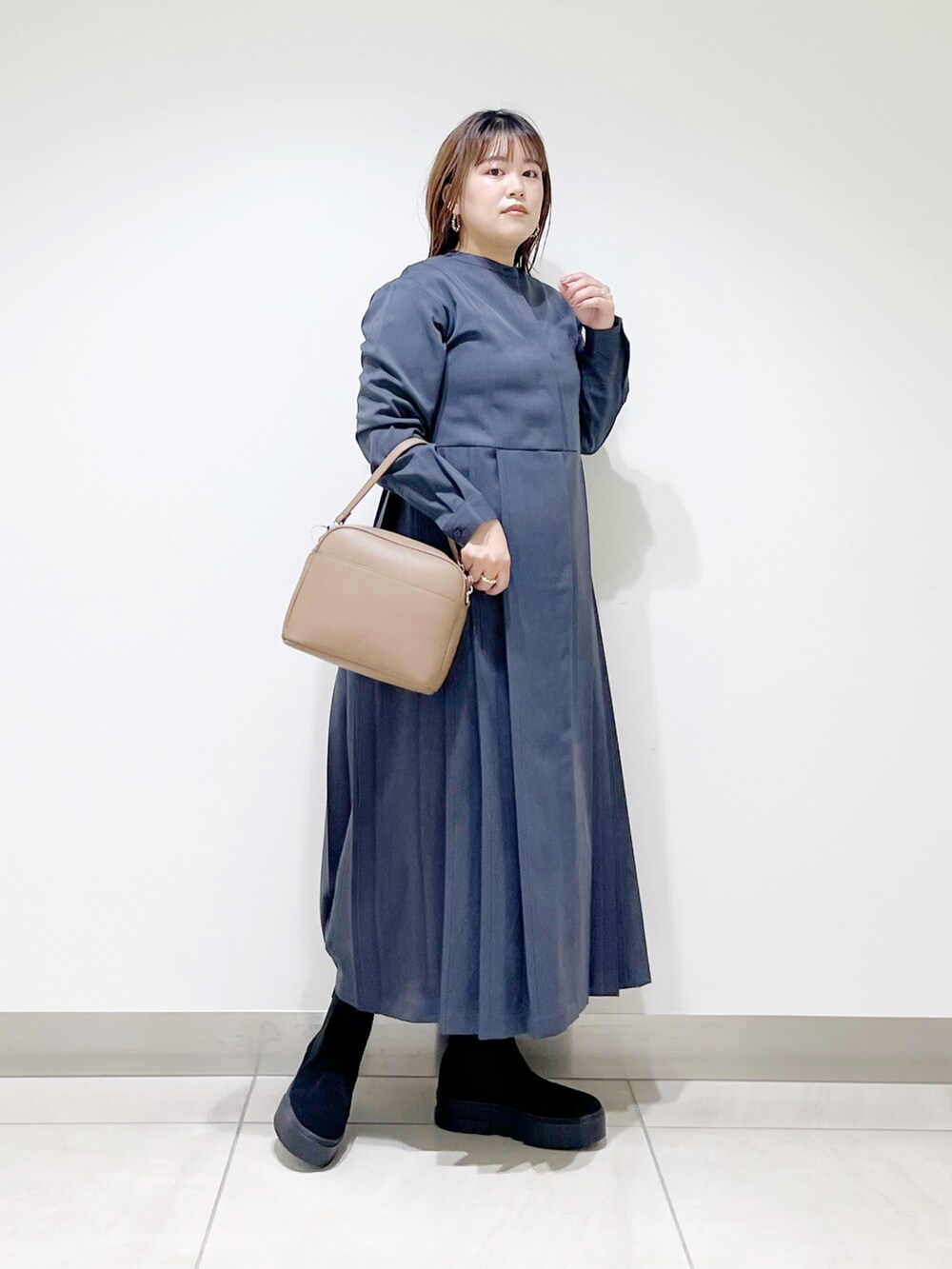 グレー系のワンピース、ブラウン系のショルダーバッグ、ブラック系のブーツを着用したレディースの秋コーディネートの2枚目の写真