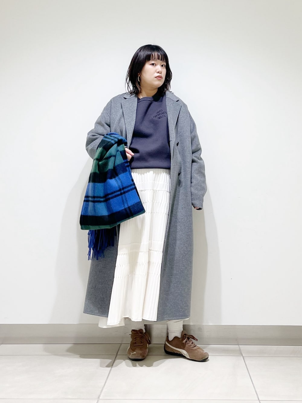 ブルー系のニット/セーター、ホワイト系のスカート、ブラック系のスニーカーを着用したレディースの秋コーディネートの10枚目の写真