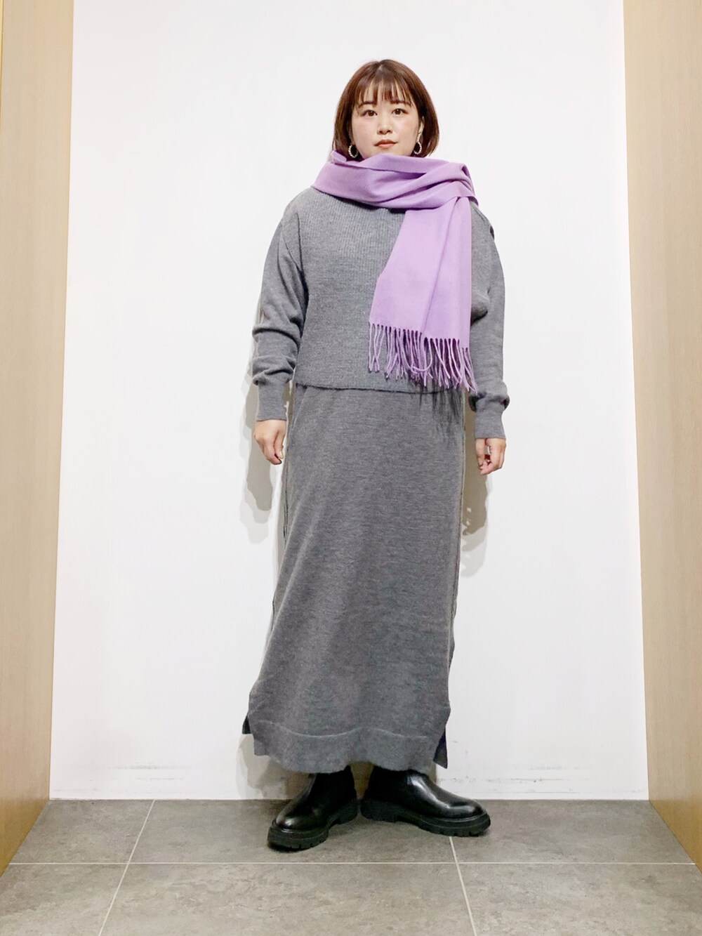 グレー系のワンピース、ブラック系のブーツ、パープル系のマフラーを着用したレディースの冬コーディネートの3枚目の写真