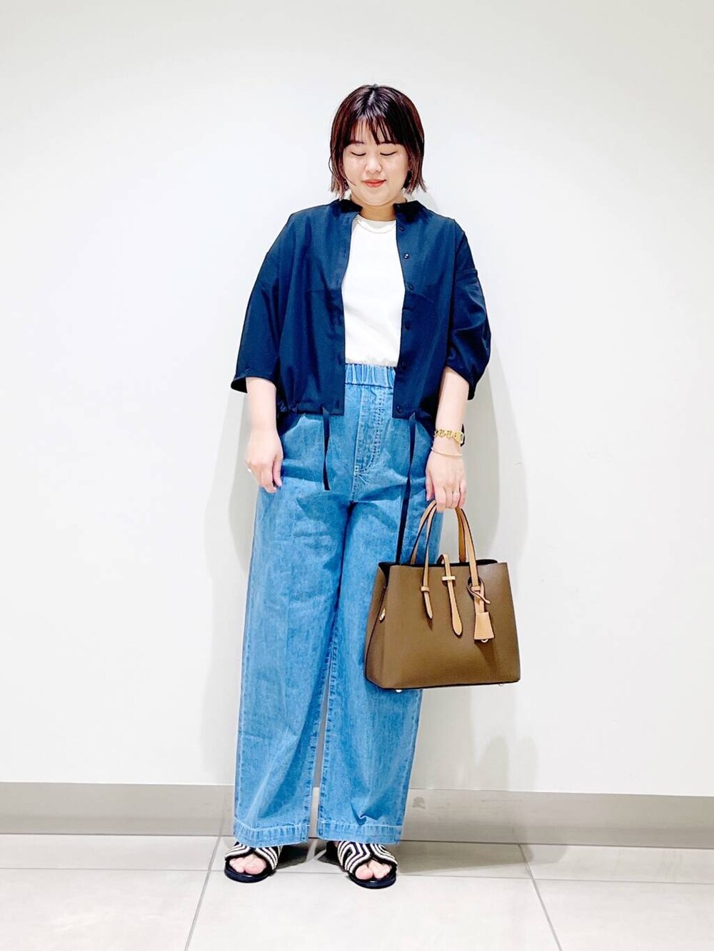 ブラウン系のトートバッグ、ブルー系のデニムパンツ、ブラック系のサンダルを着用したレディースの春コーディネートの7枚目の写真