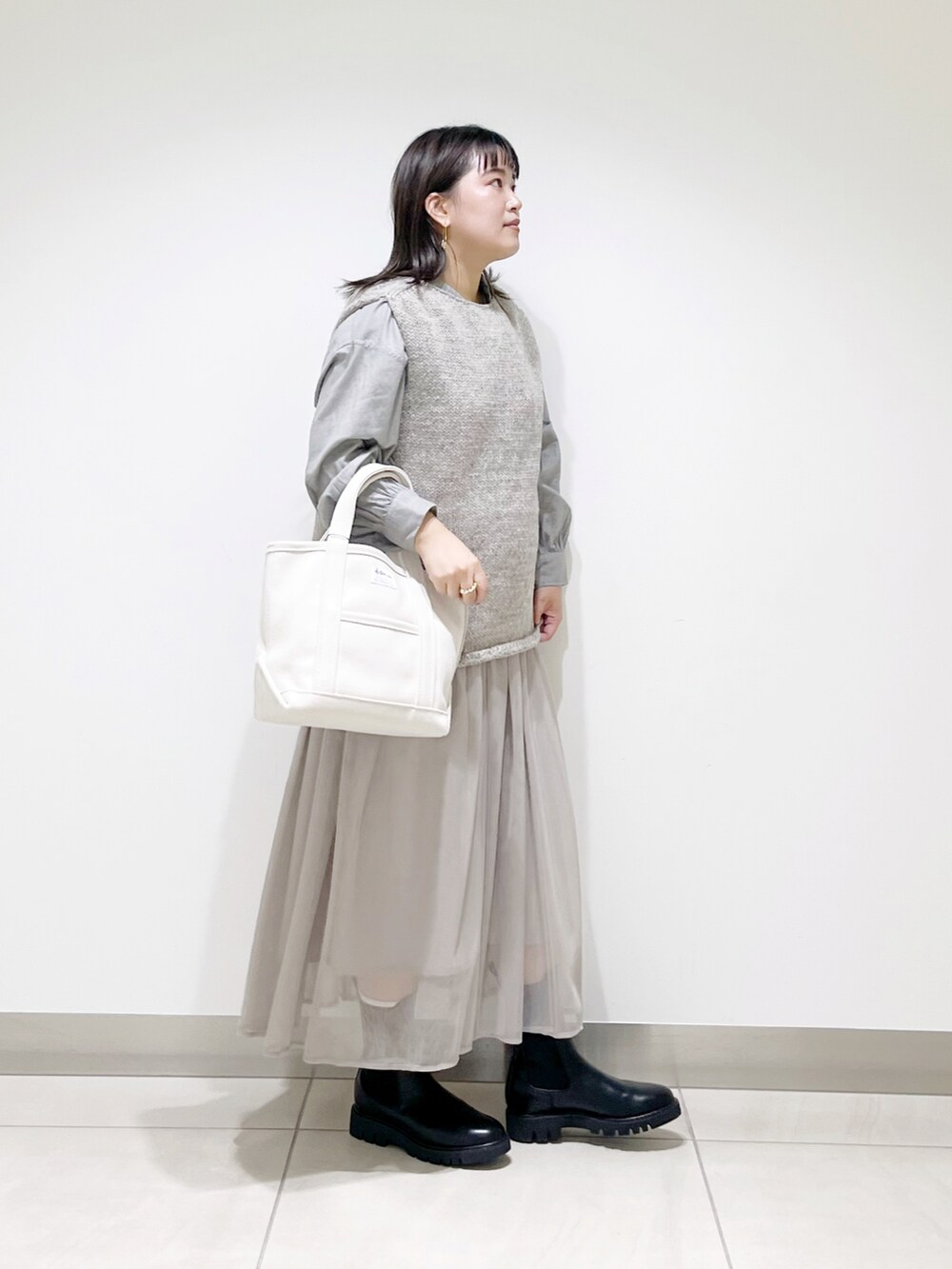 グレー系のニット/セーター、ホワイト系のトートバッグ、グレー系のスカートを着用したレディースの秋コーディネートの2枚目の写真
