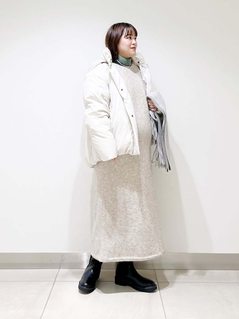 ホワイト系のダウンジャケット/コート、ベージュ系のワンピース、グリーン系のニット/セーターを着用したレディースの冬コーディネートの4枚目の写真