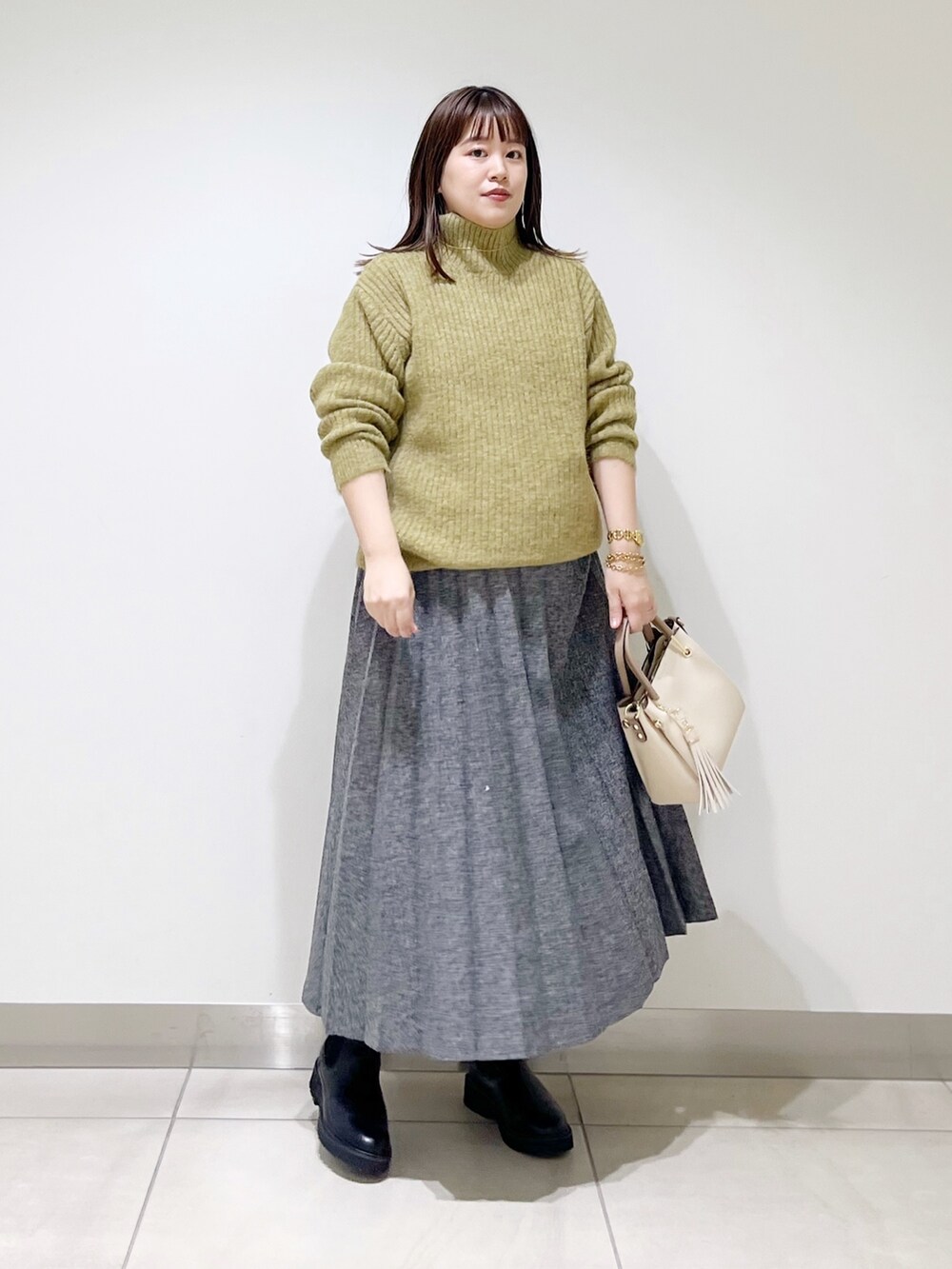 グリーン系のニット/セーター、ブルー系のスカート、ホワイト系のトートバッグを着用したレディースの冬コーディネートの3枚目の写真