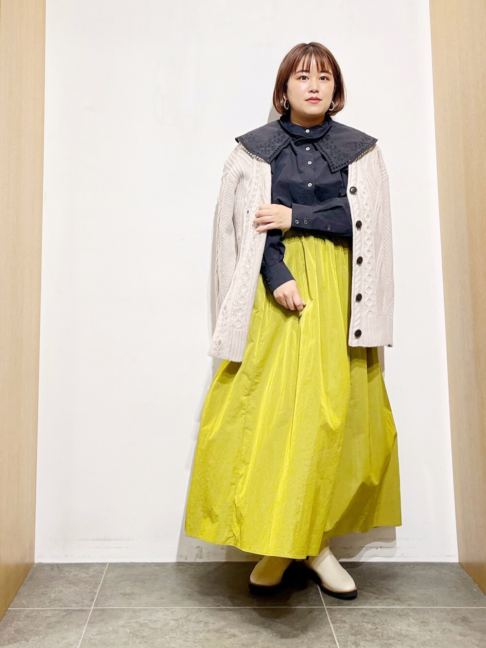 ブラック系のシャツ/ブラウス、ベージュ系のカーディガン/ボレロ、イエロー系のスカートを着用したレディースの秋コーディネートの2枚目の写真