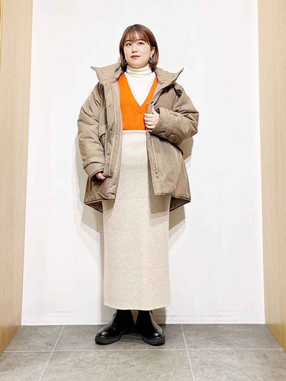 ベージュ系のダウンジャケット/コート、オレンジ系のベスト、ホワイト系のニット/セーターを着用したレディースの冬コーディネートの2枚目の写真