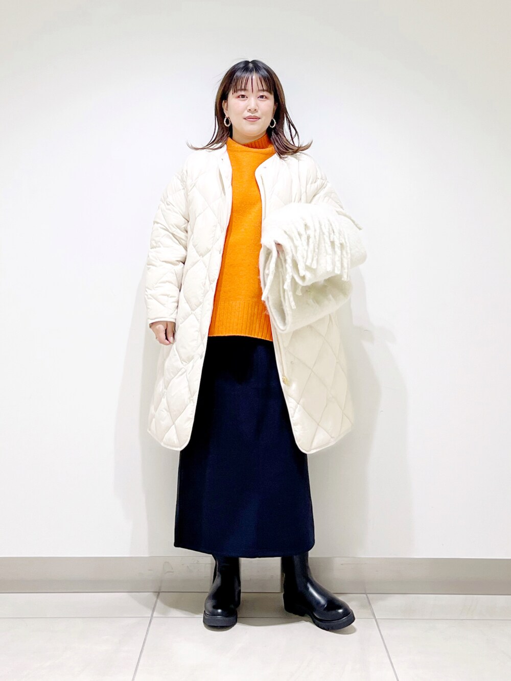 ベージュ系のダウンジャケット/コート、オレンジ系のニット/セーター、ブルー系のスカートを着用したレディースの秋コーディネートの5枚目の写真