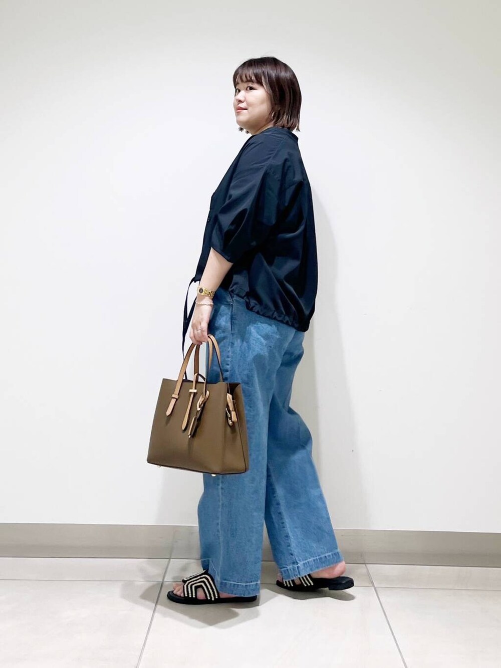 ブラウン系のトートバッグ、ブルー系のデニムパンツ、ブラック系のサンダルを着用したレディースの春コーディネートの4枚目の写真