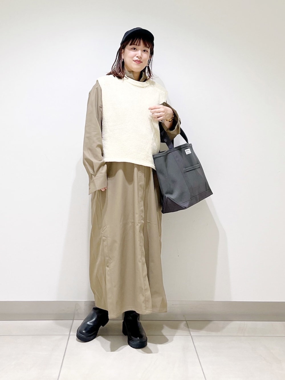 ホワイト系のベスト、グリーン系のワンピース、グレー系のトートバッグを着用したレディースの秋コーディネートの2枚目の写真