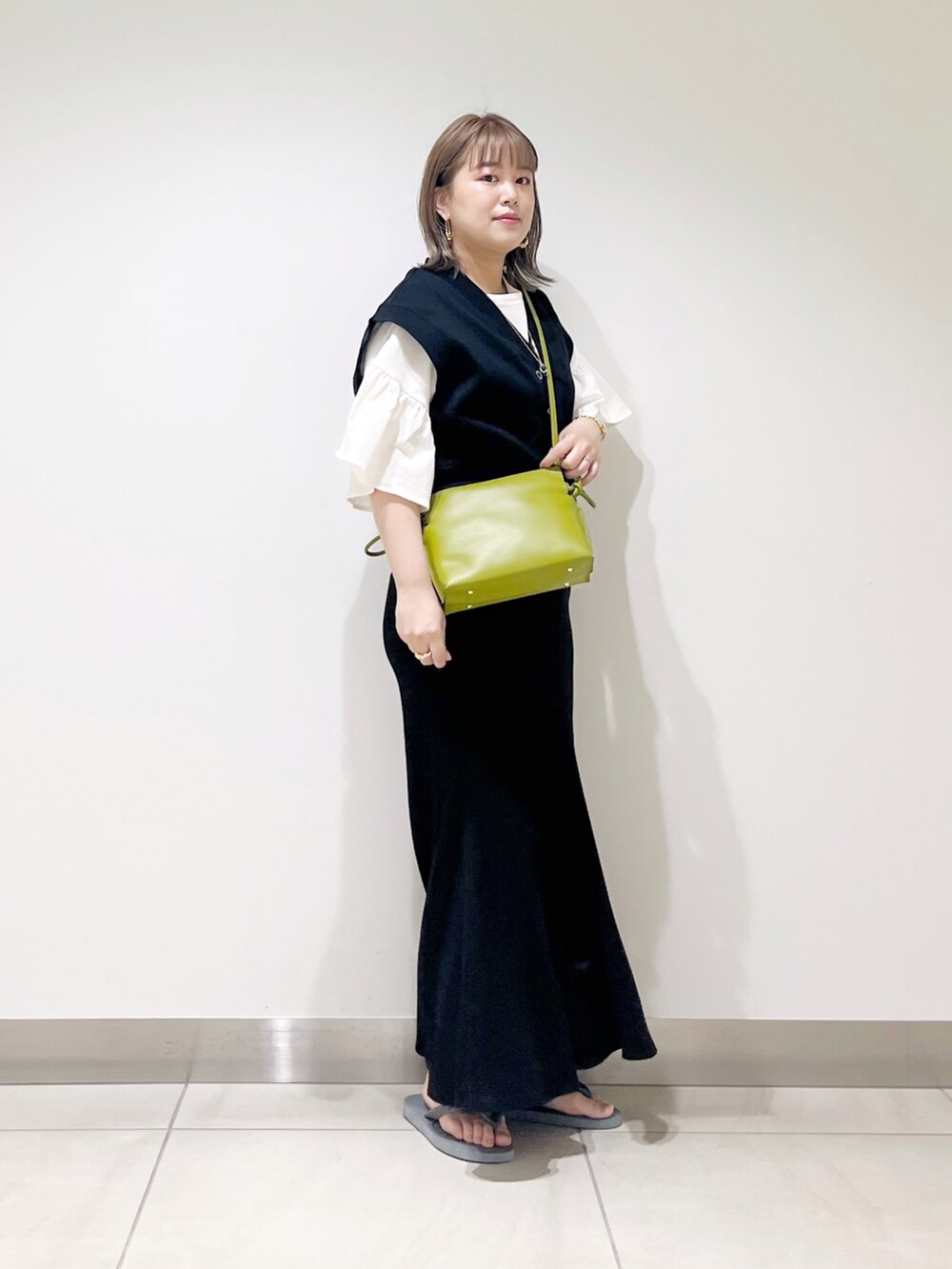 ブラック系のベスト、ブラック系のスカート、グリーン系のショルダーバッグを着用したレディースの春コーディネートの3枚目の写真