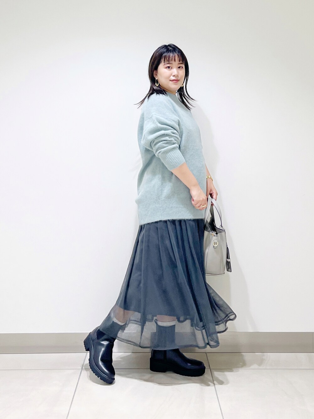 グリーン系のニット/セーター、グレー系のスカート、グレー系のトートバッグを着用したレディースの秋コーディネートの5枚目の写真