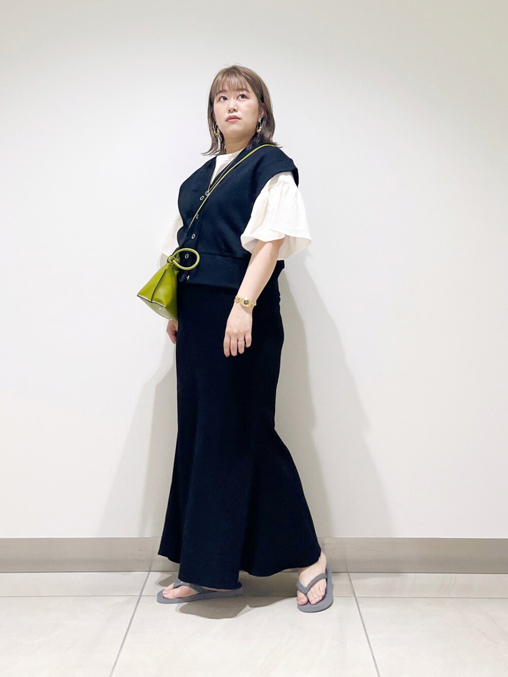 ブラック系のベスト、ブラック系のスカート、グリーン系のショルダーバッグを着用したレディースの春コーディネートの5枚目の写真