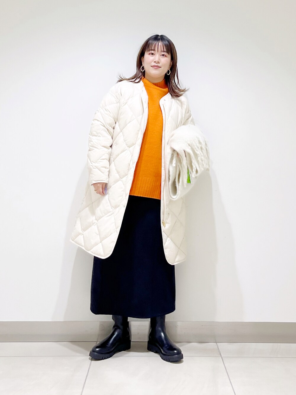 ベージュ系のダウンジャケット/コート、オレンジ系のニット/セーター、ブルー系のスカートを着用したレディースの秋コーディネートの2枚目の写真