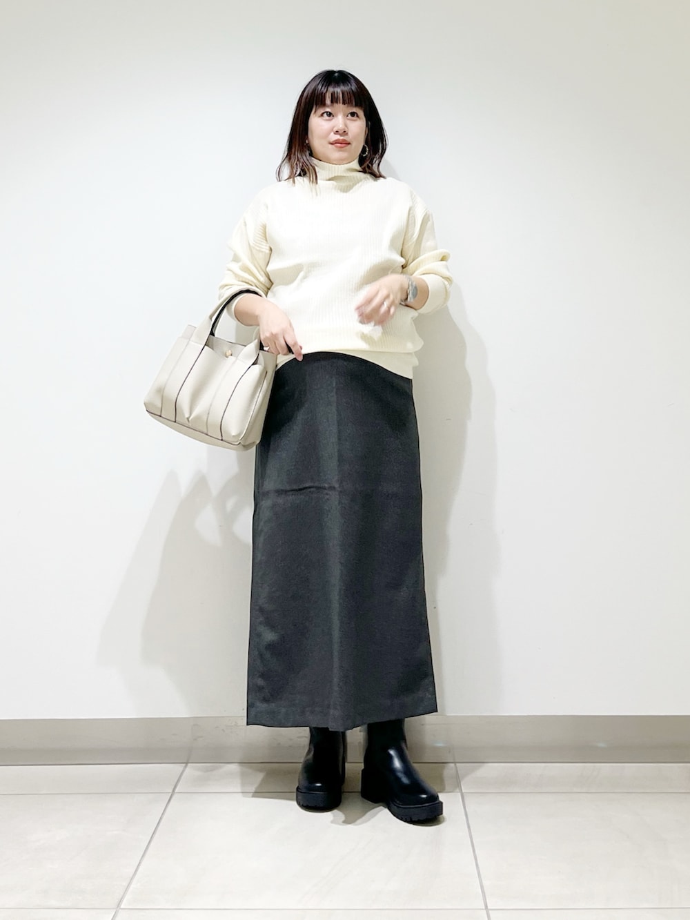 ホワイト系のニット/セーター、ホワイト系のトートバッグ、グレー系のスカートを着用したレディースの秋コーディネートの3枚目の写真